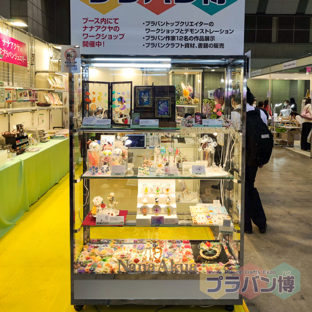 作品展示ショーケースの写真。12名のうち9名の作品がガラスショーケースに入って照明で浮かび上がっている